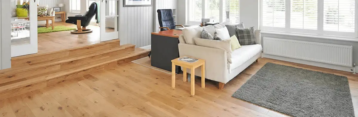 A modern living room with professionally installed laminate flooring, a beige sofa, a small side table, a gray rug, and large windows with white shutters in Stockton, CA